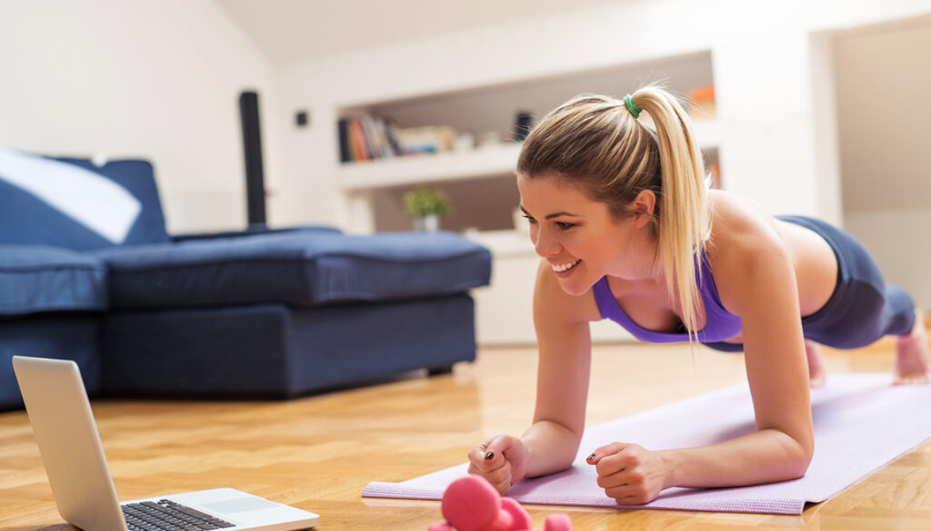 Young girl looking at laptop and doing exercises at home.