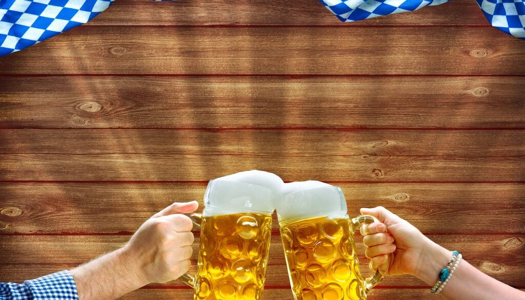 Hands holding up beer mugs under Bavarian flag