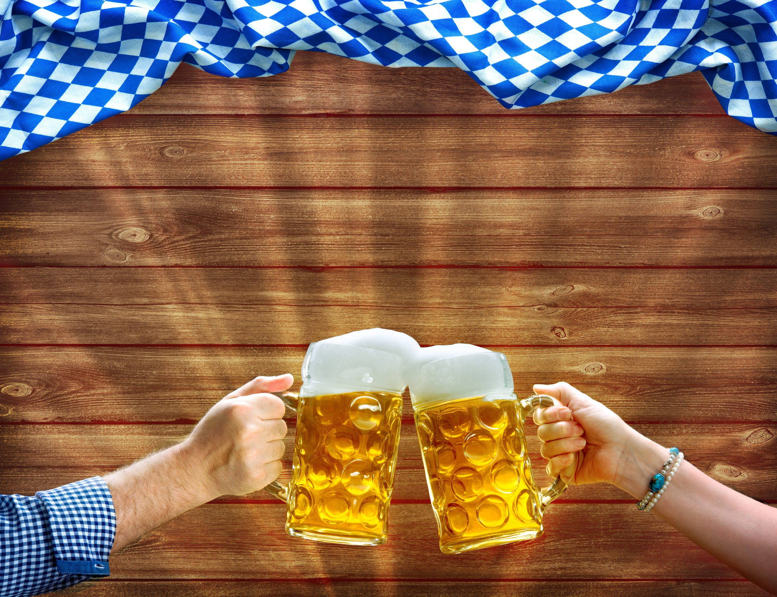 Hands holding up beer mugs under Bavarian flag
