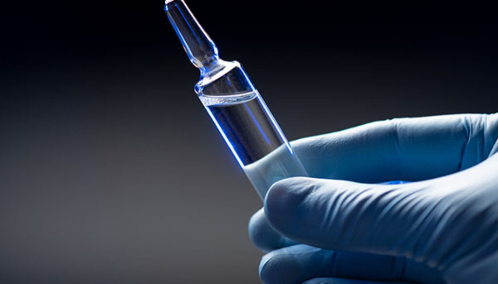 Hand in blue medical gloves holds an ampoule with a coronavirus vaccine.