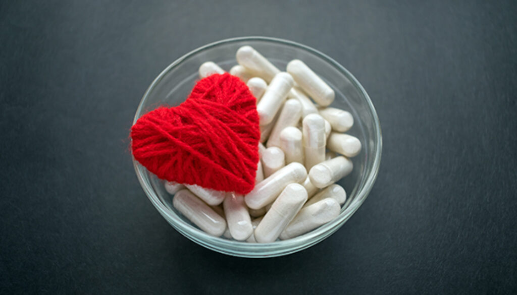 White veg capsules and red thread heart in glass bowl on black b